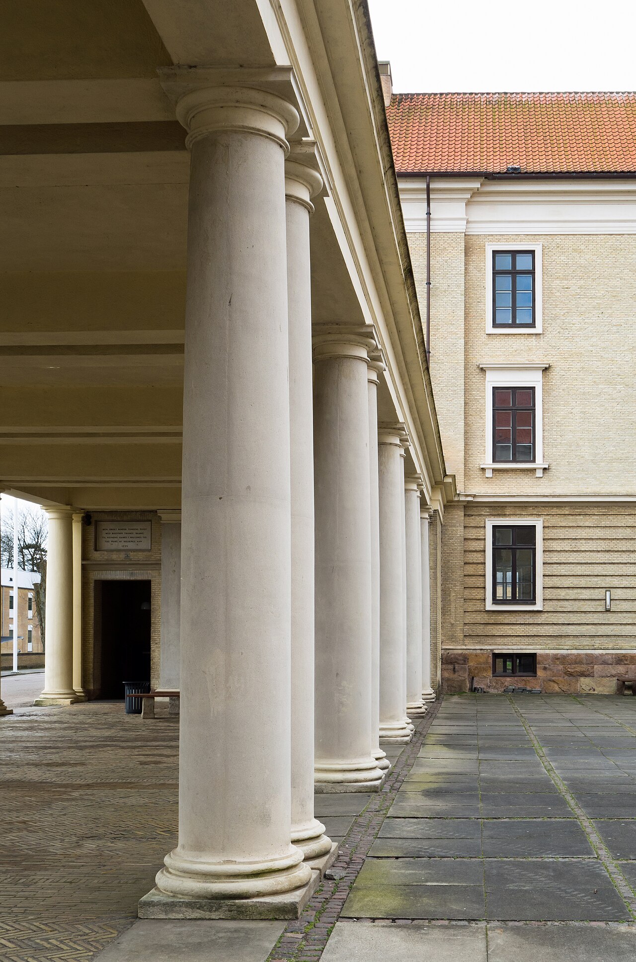 Pale columns beside a covered walkway, with a dark doorway at the far end.