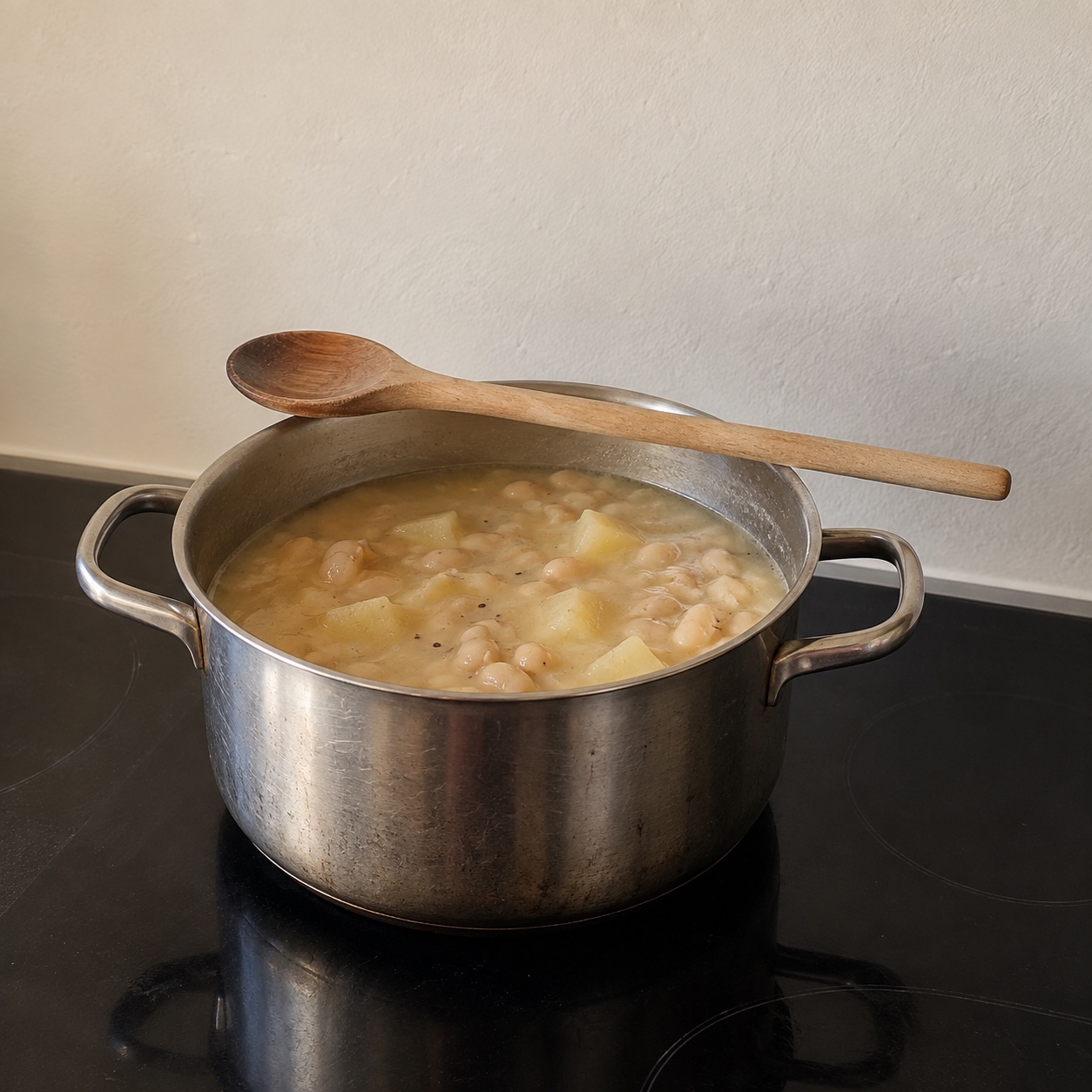 A steel pot of soup on a stove with a wooden spoon resting across the rim. Shared by Amara.