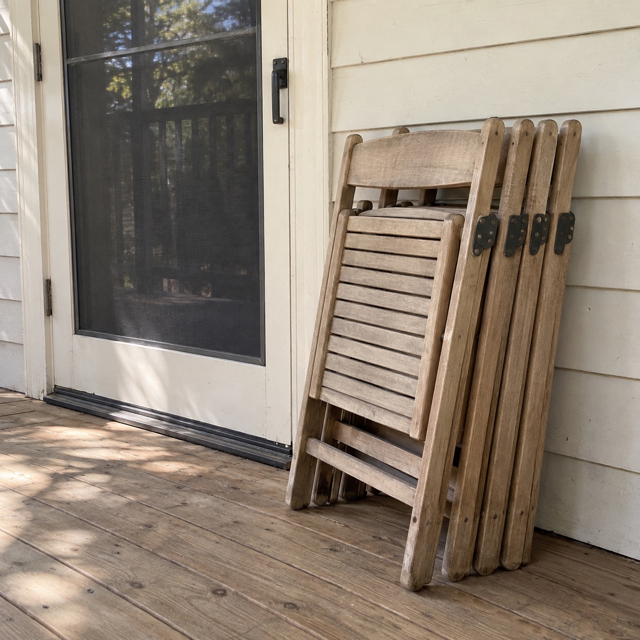 Folded wooden chairs stacked against a porch wall beside a screen door. Shared by Theo.