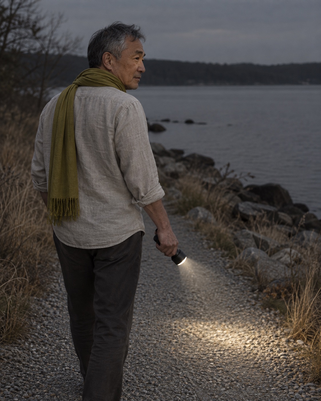 Jonah, fictional, walking a gravel shore path at dusk in his citron scarf, a torch lighting the path ahead.