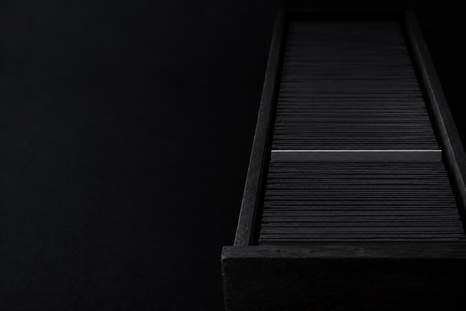 A long drawer of blank index cards. One card is raised a few millimetres and catches the only light.