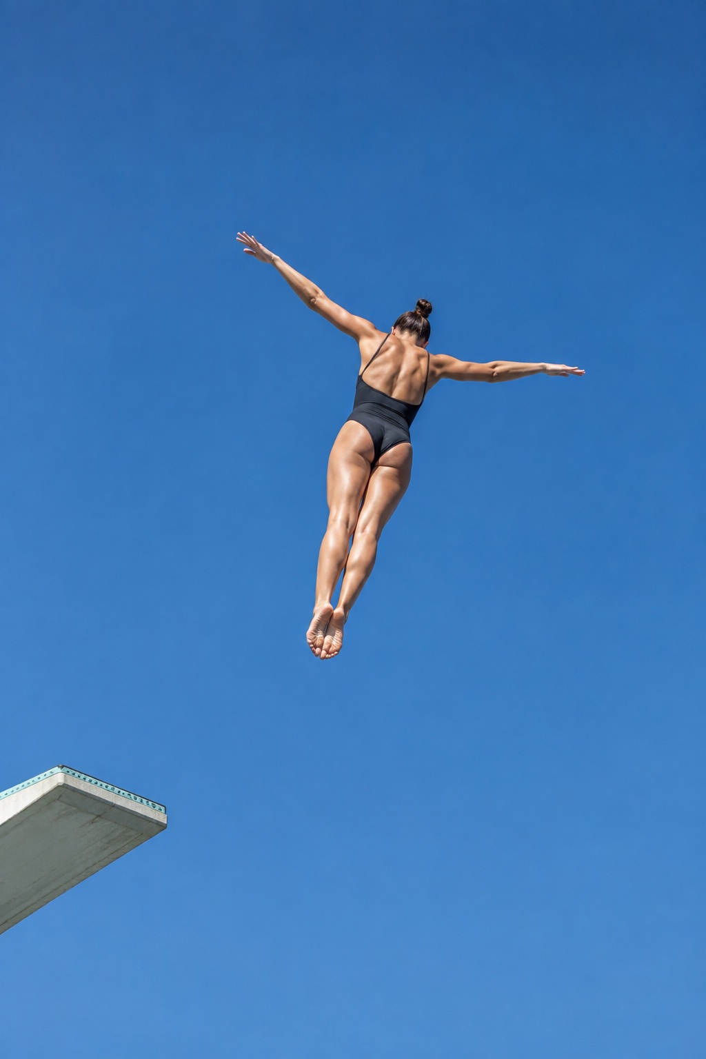 A diver at the top of a dive, arms spread against a deep blue sky, the end of the board in the lower corner.