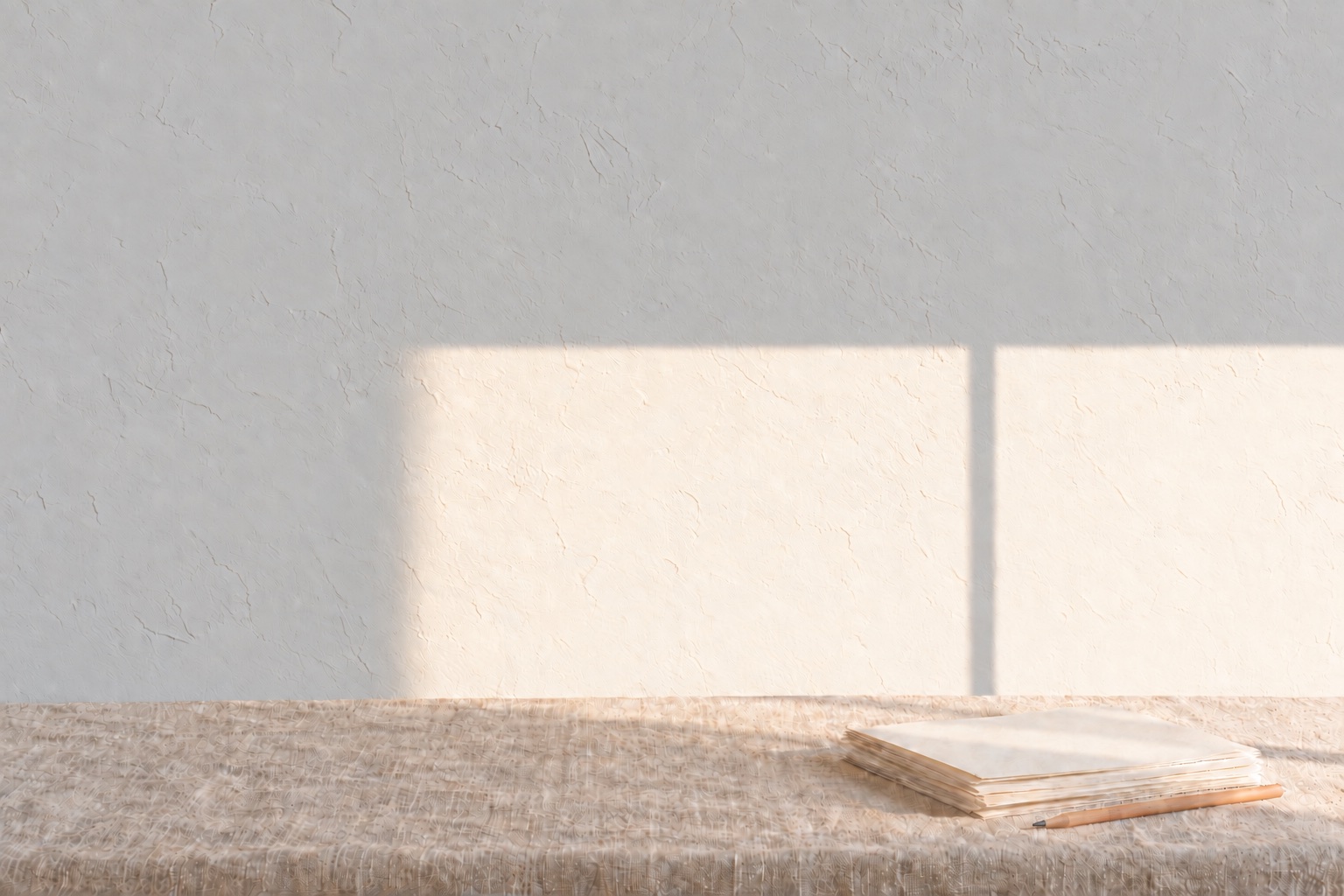 Bright morning sun through a window, split by the mullion’s shadow, on a limewashed wall above a linen table with a stack of loose pages and a pencil.